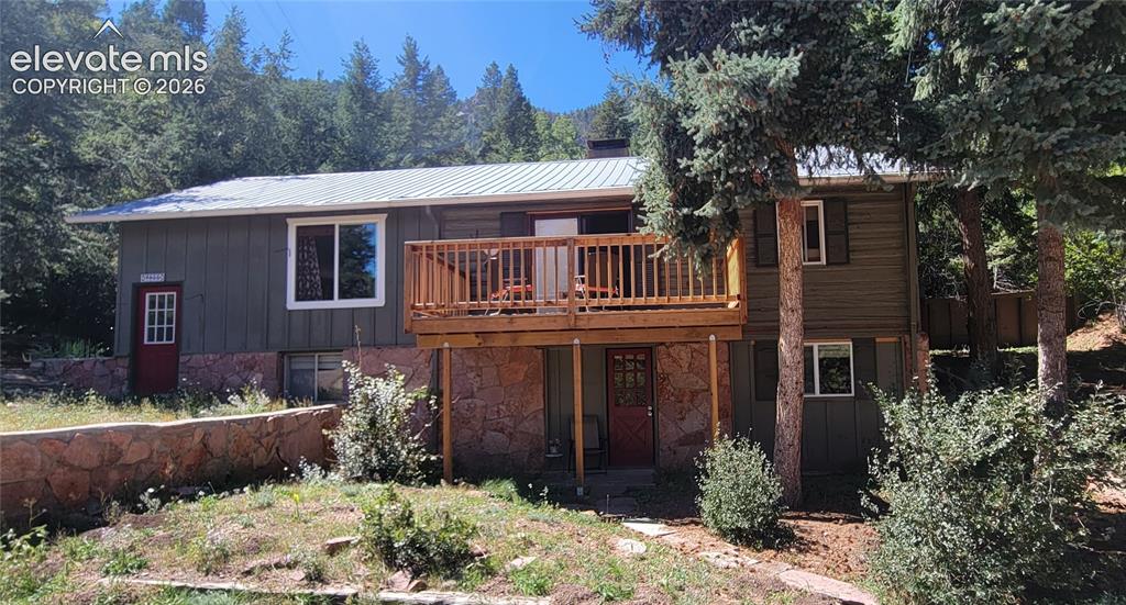 Caption: Two-story exterior with a metal roof, wood siding, natural stone foundation accent, and a wood deck