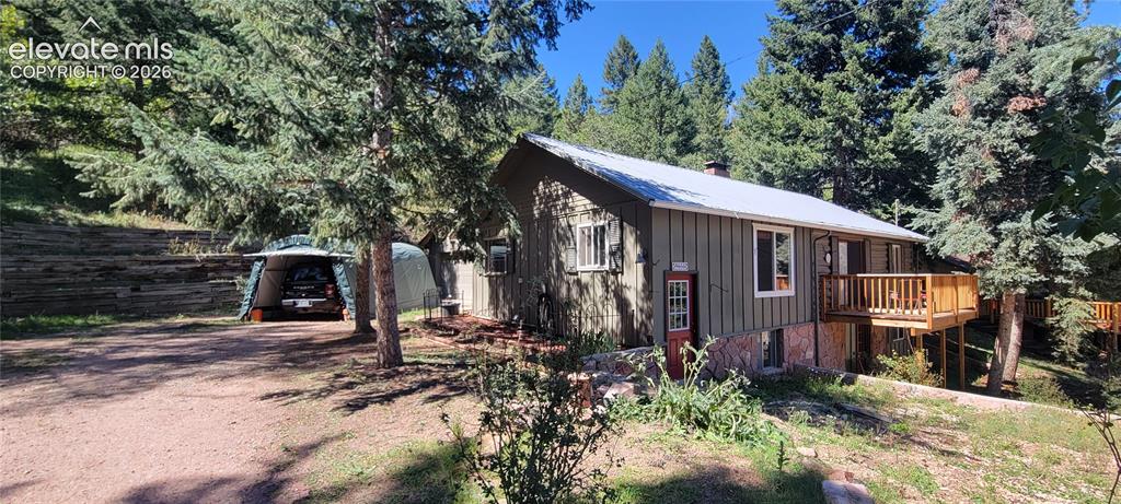 Image 2 of 30: Wood-sided residence with a metal roof, elevated wood deck, and a gravel dr