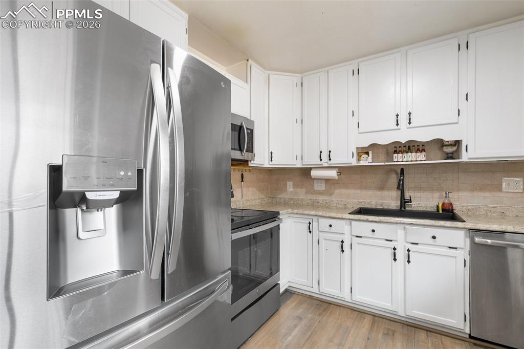 Image 11 of 29: Kitchen featuring stainless steel appliances, white cabinets, open shelves,