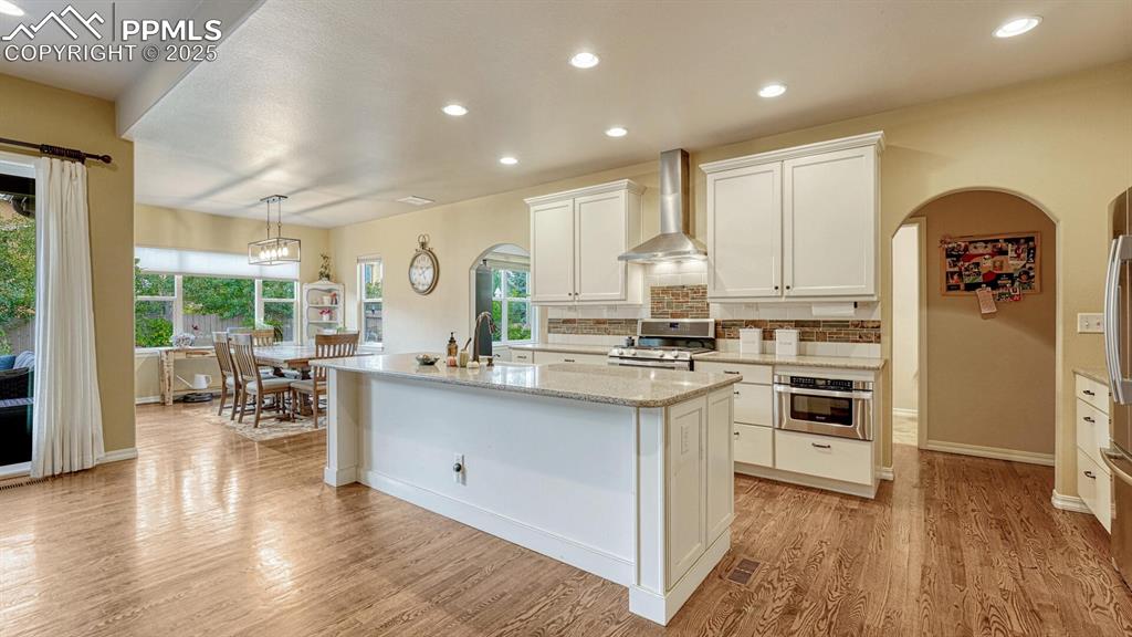 Image 11 of 44: Kitchen with arched walkways, recessed lighting, wall chimney exhaust hood,