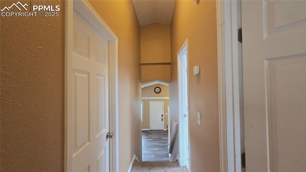 Image 25 of 42: Corridor featuring vaulted ceiling, a textured wall, carpet, and a textured