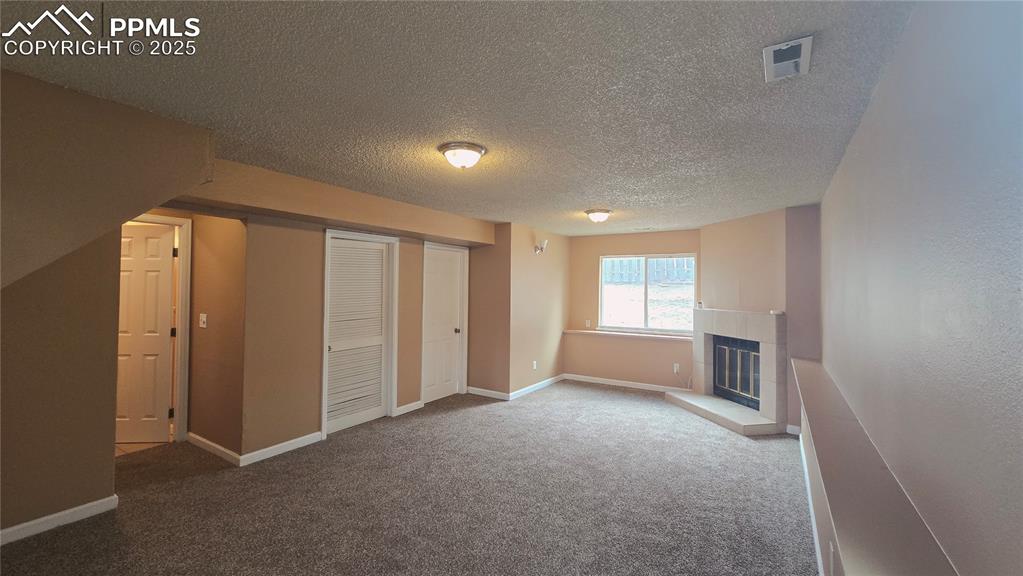 Image 32 of 42: Unfurnished living room featuring a tiled fireplace, carpet flooring, and a