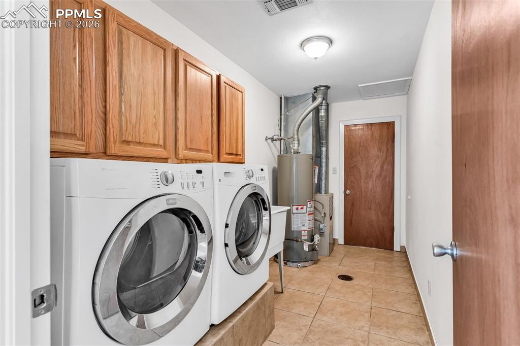 Image 24 of 42: Laundry room featuring washer and clothes dryer, gas water heater, cabinet 