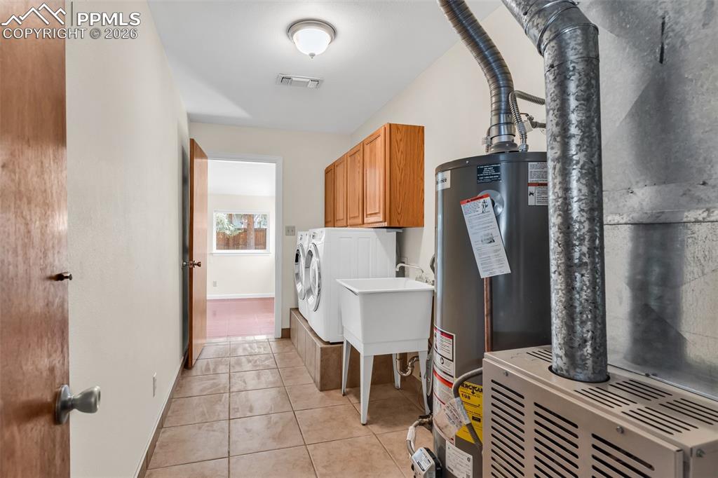 Image 25 of 42: Laundry area with washing machine and dryer, cabinet space, gas water heate