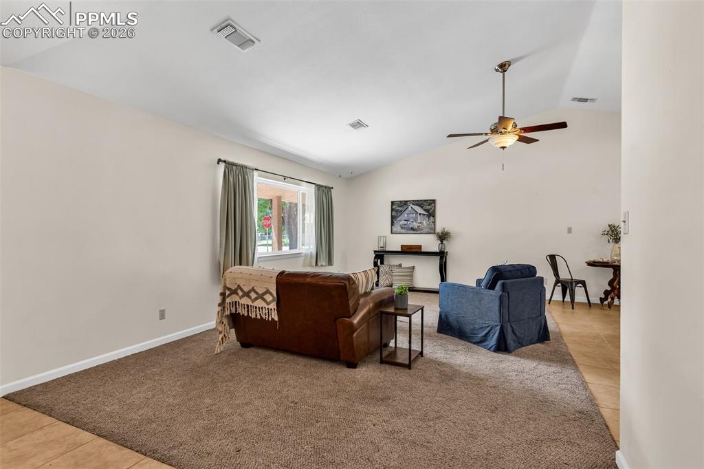 Image 4 of 42: Tiled living area with vaulted ceiling, ceiling fan, carpet flooring, and b