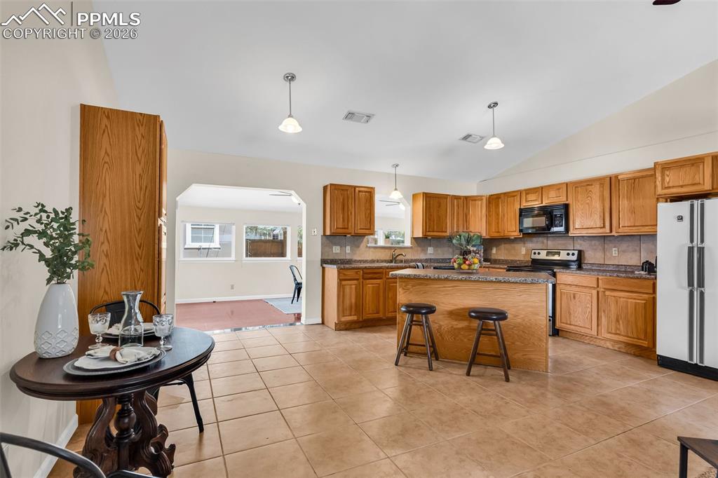 Image 9 of 42: Kitchen featuring black microwave, freestanding refrigerator, vaulted ceili