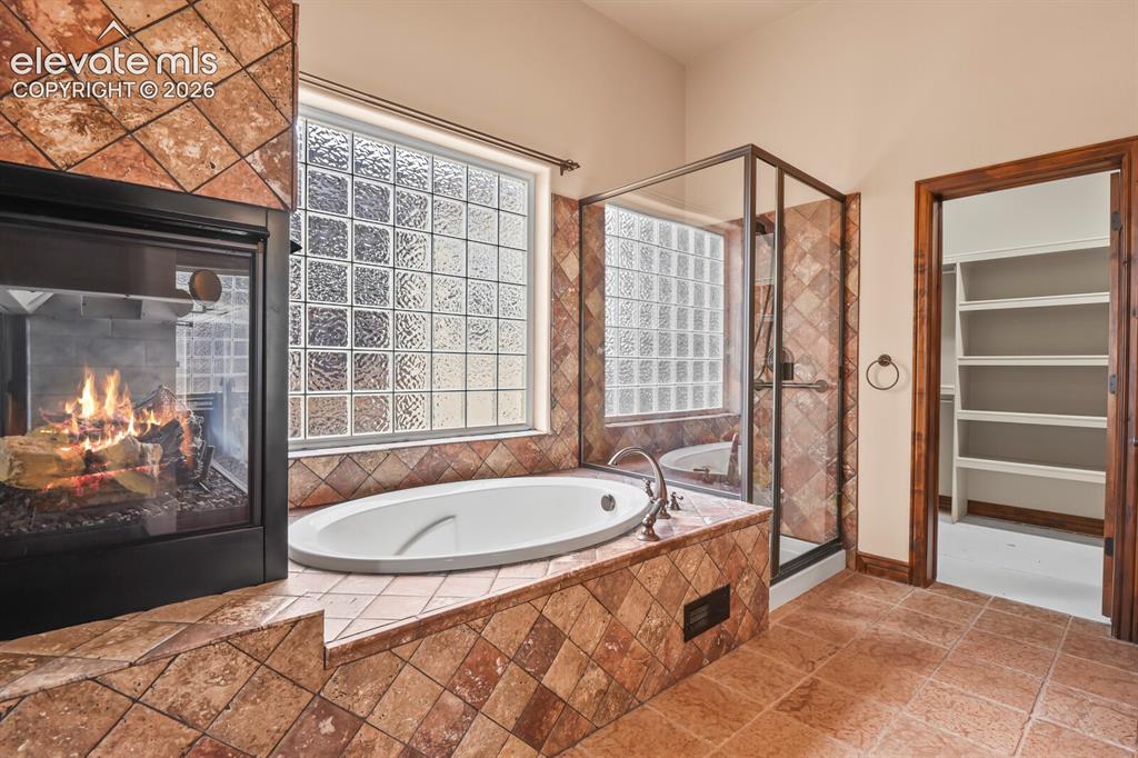 Image 19 of 33: Elegant soaking tub with custom tile work and gas fireplace, freestanding,