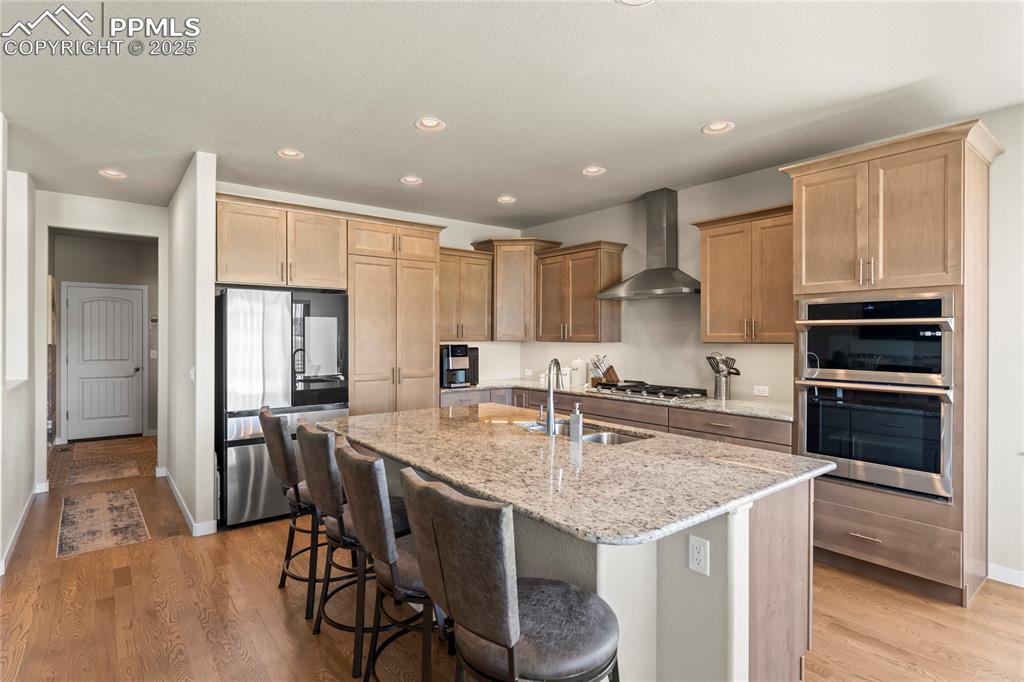 Image 15 of 50: Kitchen with stainless steel appliances, wall chimney range hood, light sto