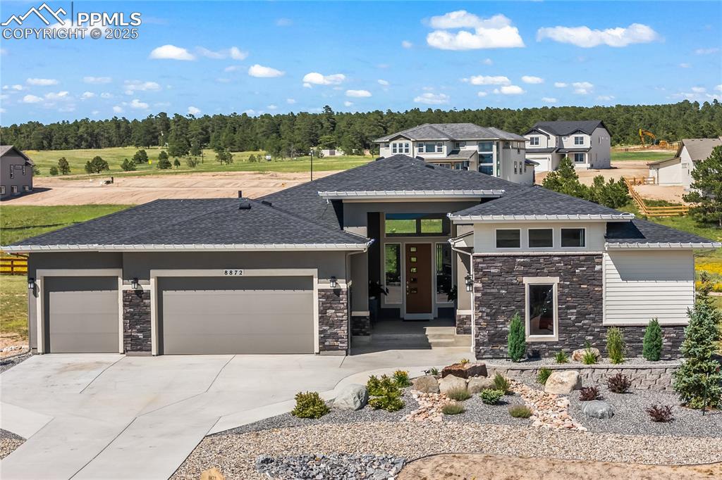 Image 2 of 50: Prairie-style home featuring stone siding, an attached garage, concrete dri