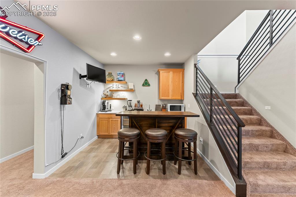 Image 39 of 50: Indoor wet bar featuring white microwave, stairway, recessed lighting, and