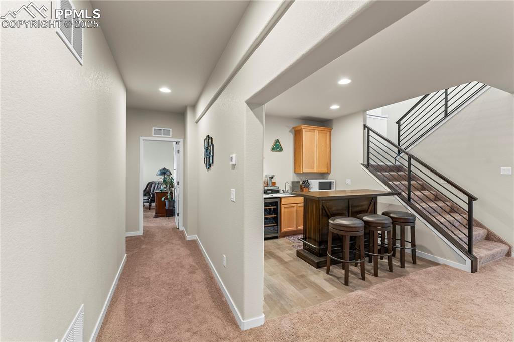 Image 43 of 50: Indoor bar featuring light carpet, white microwave, recessed lighting, stai