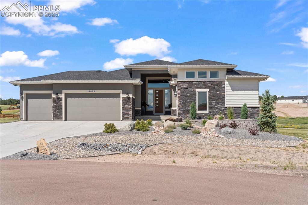 Image 7 of 50: Prairie-style home featuring stone siding, a garage, concrete driveway, and