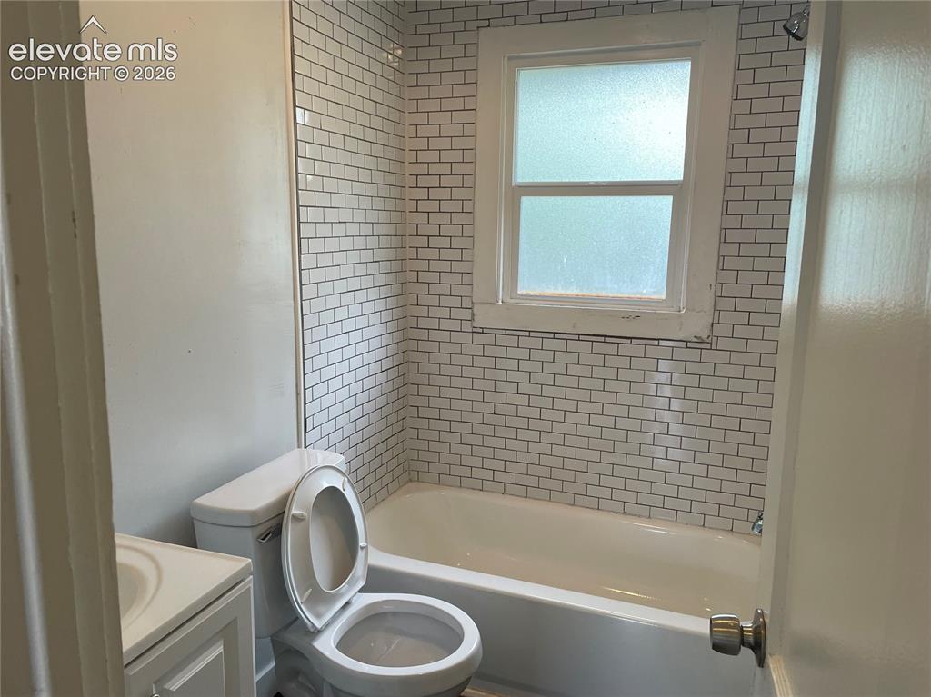Image 6 of 16: Bathroom featuring a white subway tile surround, white bathtub, and a windo