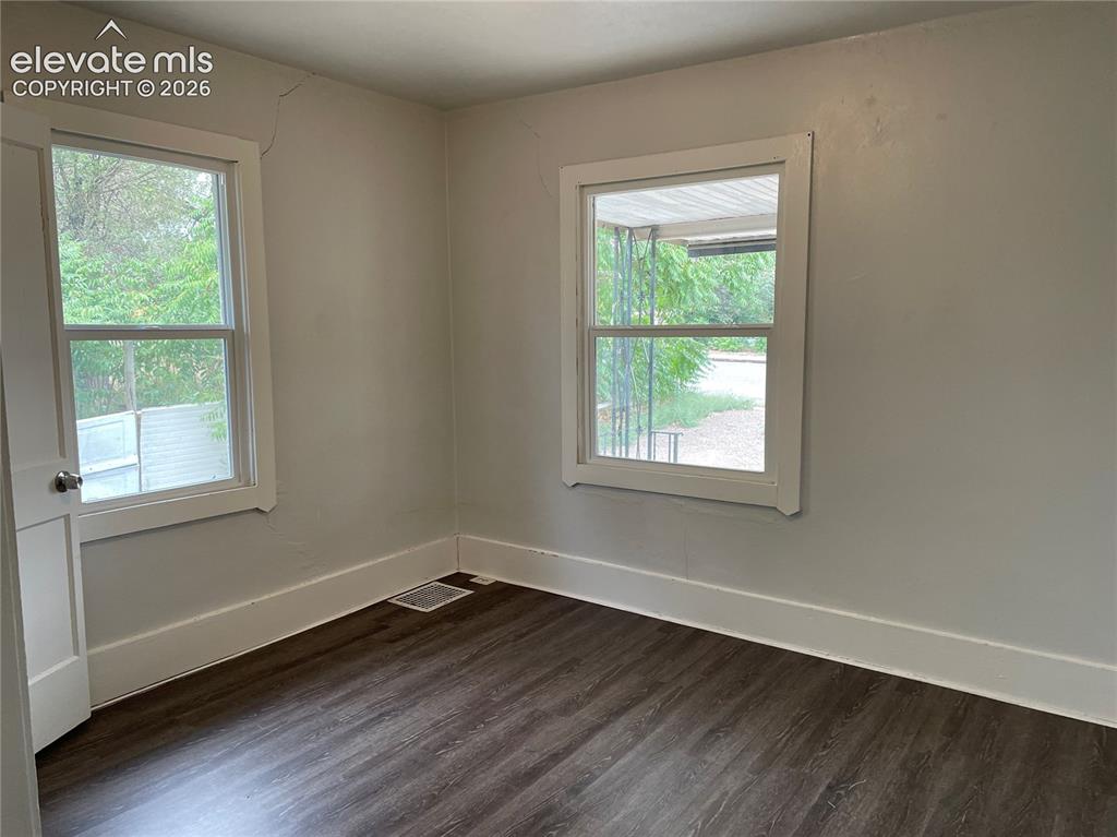 Image 7 of 16: Room with dark wood-finish flooring and two windows with white trim