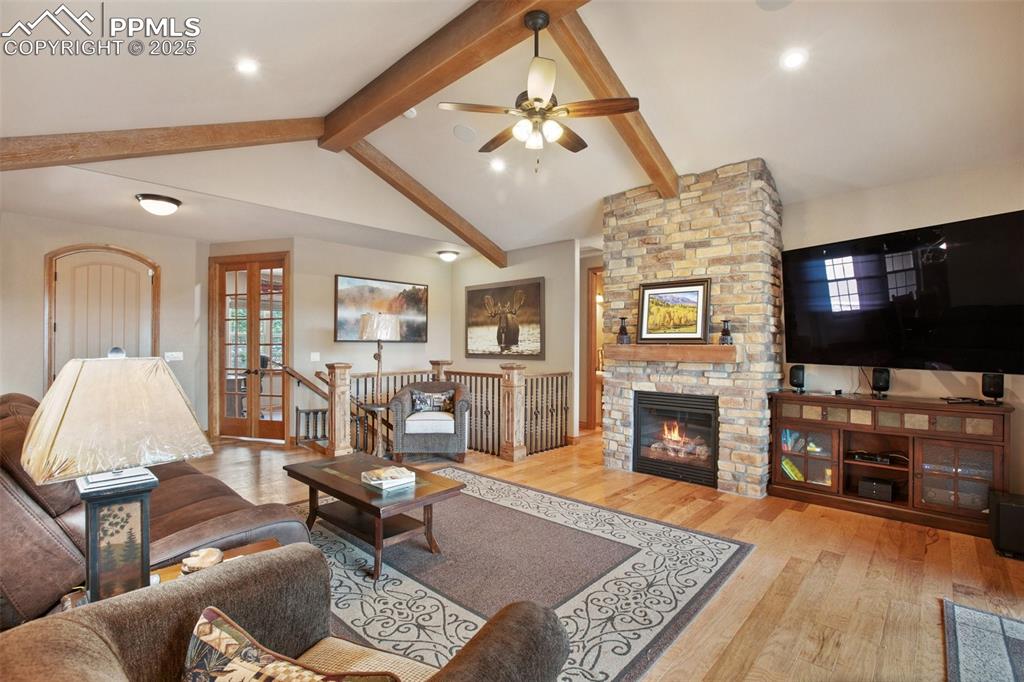 Image 17 of 48: Living room featuring ceiling fan, lofted ceiling with beams, a stone firep