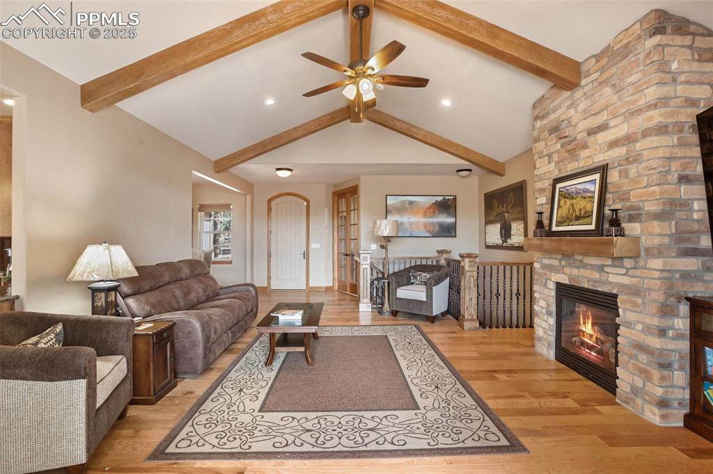 Image 19 of 48: Living room featuring beam ceiling, ceiling fan, a fireplace, and light woo