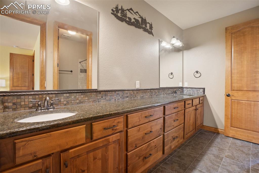 Image 28 of 48: Bathroom with double vanity, baseboards, backsplash, and a sink