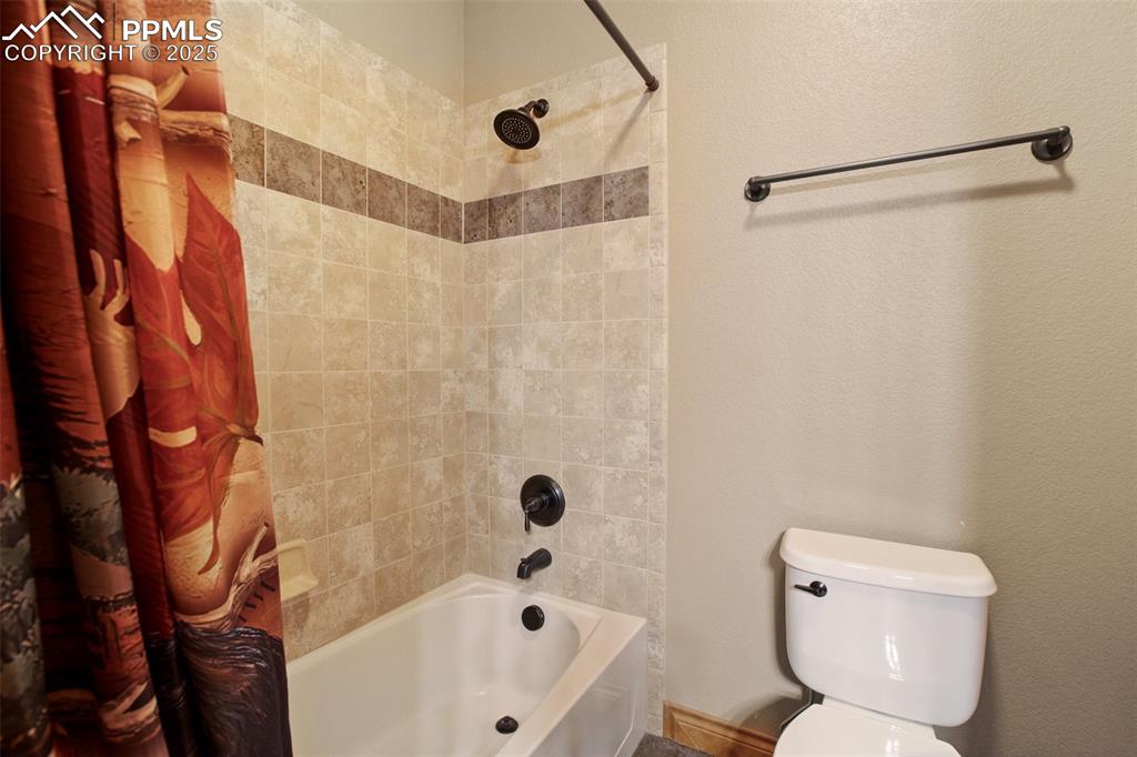 Image 29 of 48: Bathroom with a textured wall, toilet, and shower / bath combination with c