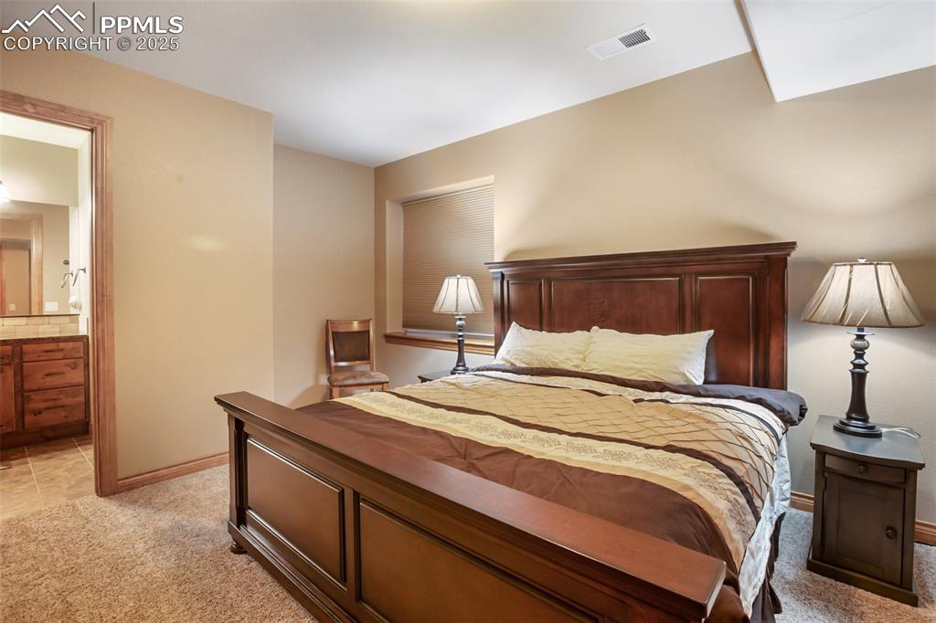Image 41 of 48: Bedroom with visible vents, baseboards, light colored carpet, and ensuite b