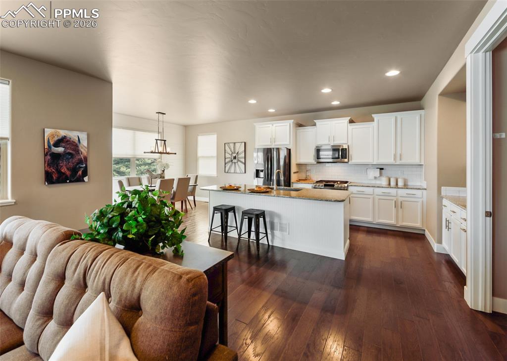 Image 11 of 50: Open-concept living area featuring rich wood-finish flooring, white kitchen