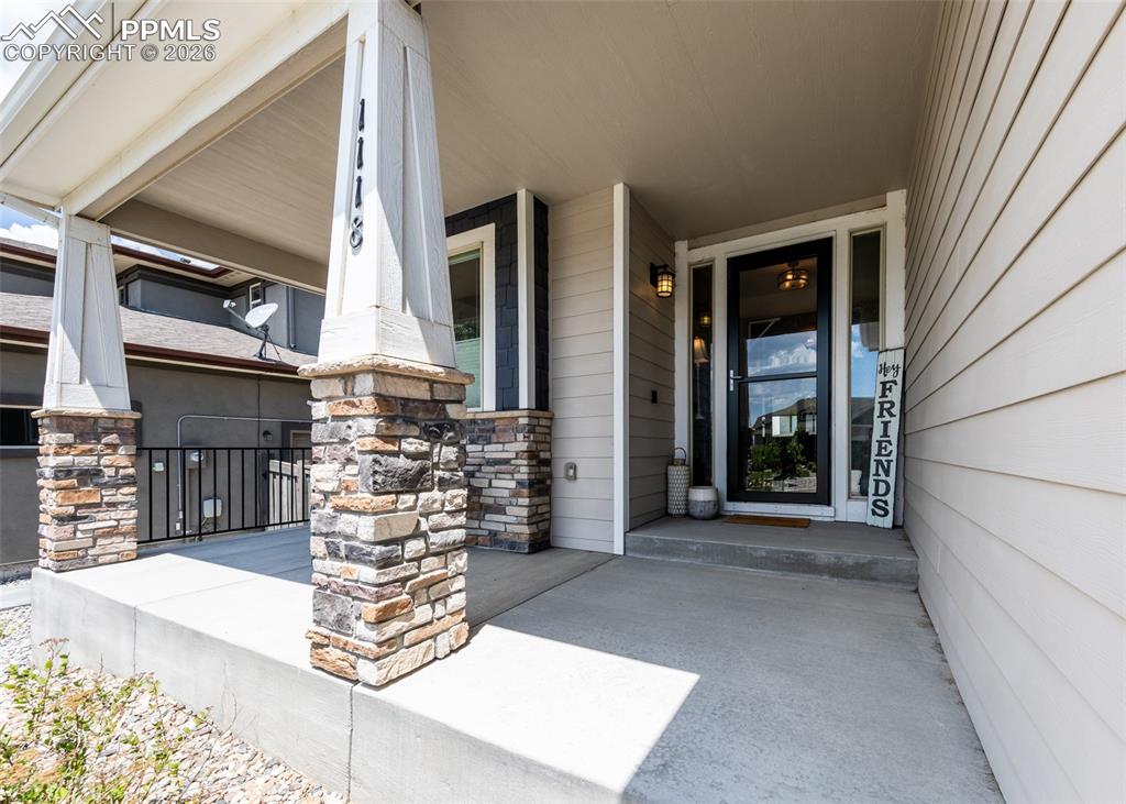 Image 3 of 50: Covered front porch featuring stacked stone-wrapped columns, concrete floor