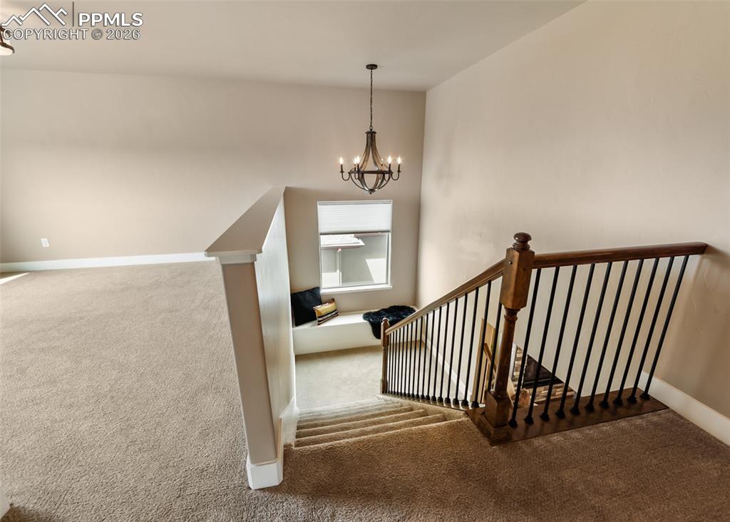 Image 30 of 50: Carpeted landing featuring a wooden chandelier, window seat, and staircase