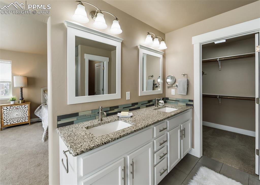 Image 37 of 50: Dual vanity with undermount sinks, speckled countertop, and a tiled backspl