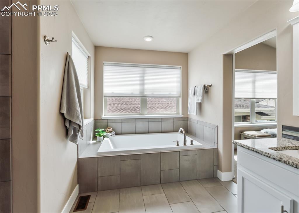 Image 38 of 50: Soaking tub with tile surround, dual windows with blinds, recessed lighting