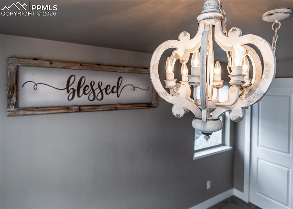 Image 43 of 50: Distressed white chandelier illuminating a neutral-toned wall, featuring a