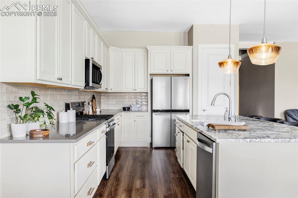 Image 9 of 44: Kitchen with stainless steel appliances, light stone counters, dark wood-st