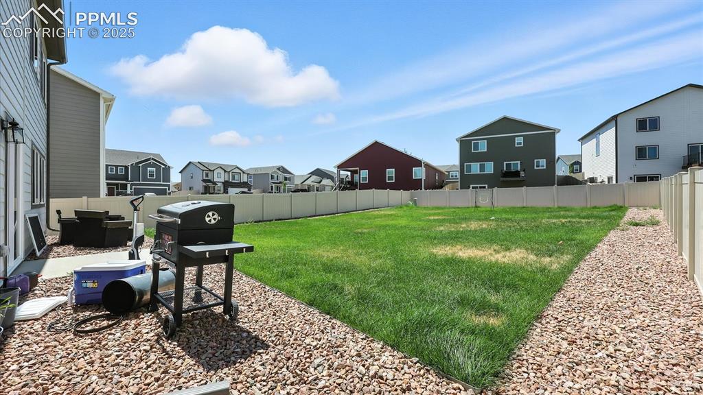 Image 18 of 50: View of the fenced backyard with xeriscaped rock gardens and green grass.