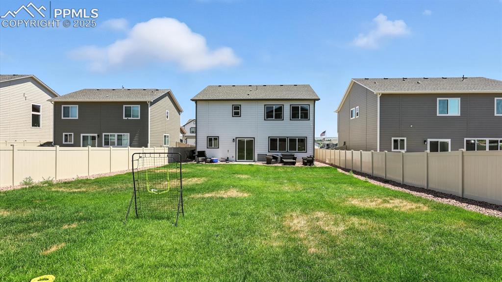 Image 46 of 50: Spacious fenced backyard with concrete patio, rock beds, and lush green gra