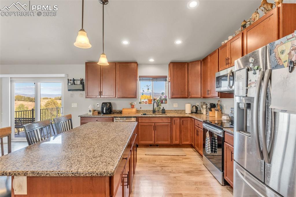 Image 13 of 37: Kitchen featuring stainless steel appliances, brown cabinets, light stone c