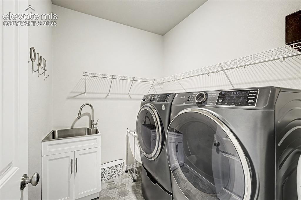 Image 22 of 45: Convenient main-level laundry room with cabinetry and utility sink keeps e
