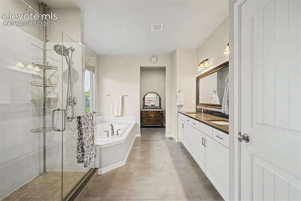 Image 26 of 45: Luxurious primary bath features dual vanities, an oversized glass-enclosed 