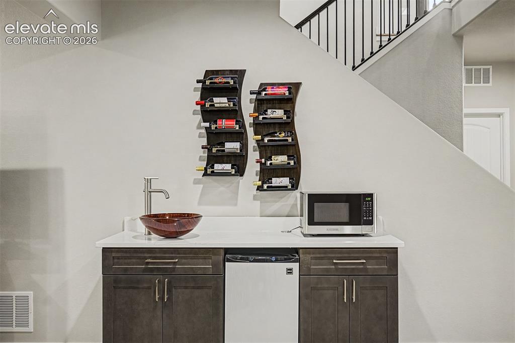Image 29 of 45: Basement wet bar features custom wine shelving, cabinetry, and a beverage r
