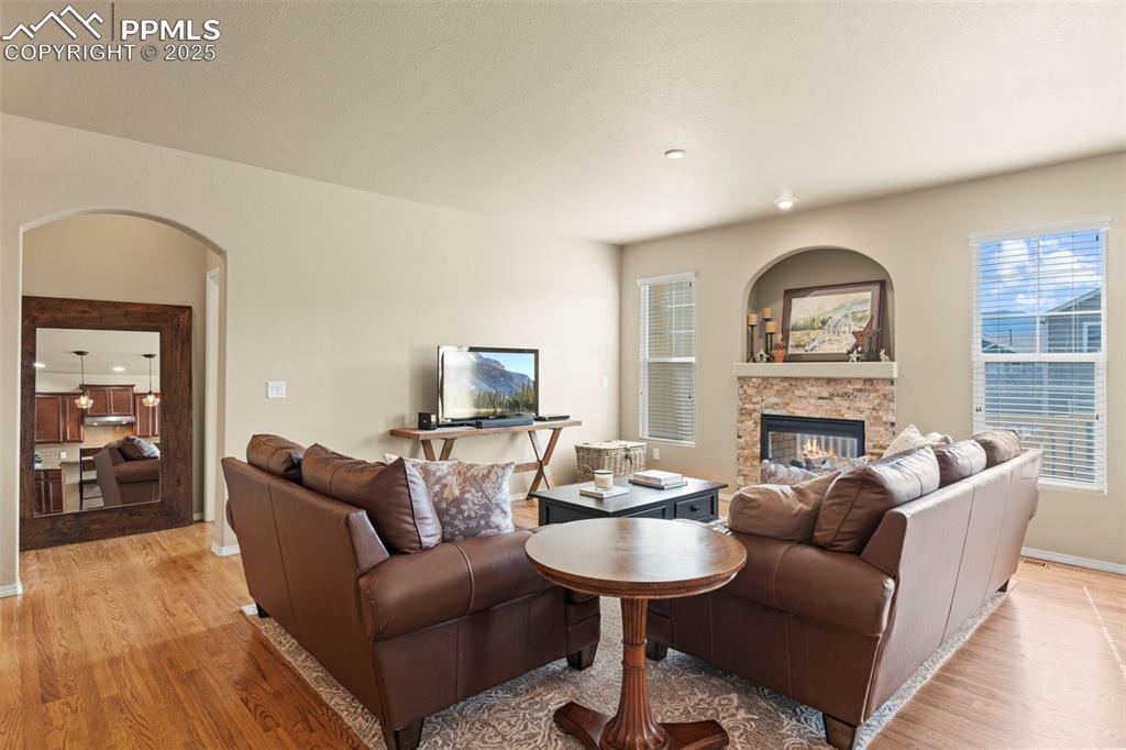 Image 10 of 44: Living room featuring arched walkways, light wood-type flooring, a stone fi