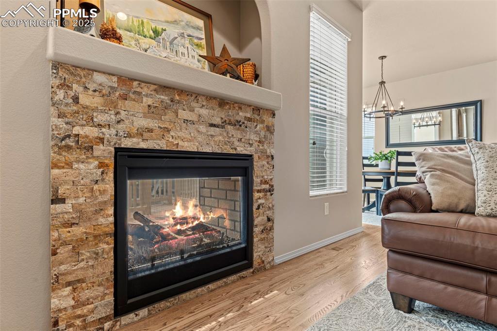 Image 12 of 44: Living area with a chandelier, wood finished floors, baseboards, and a fire