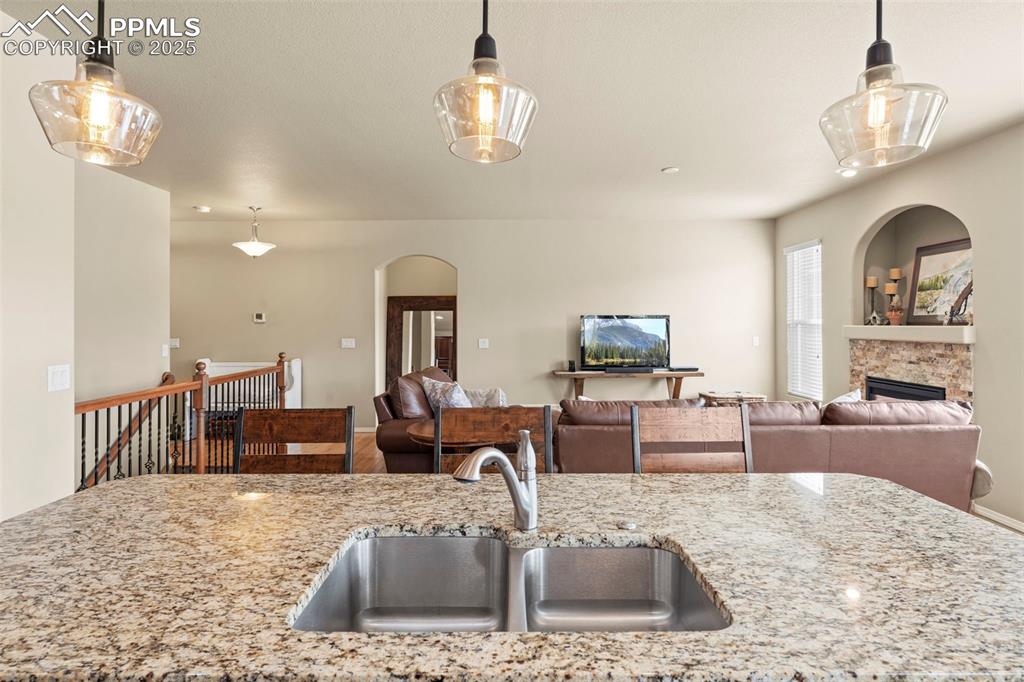Image 18 of 44: Kitchen with a sink, a fireplace, light stone counters, and pendant lightin
