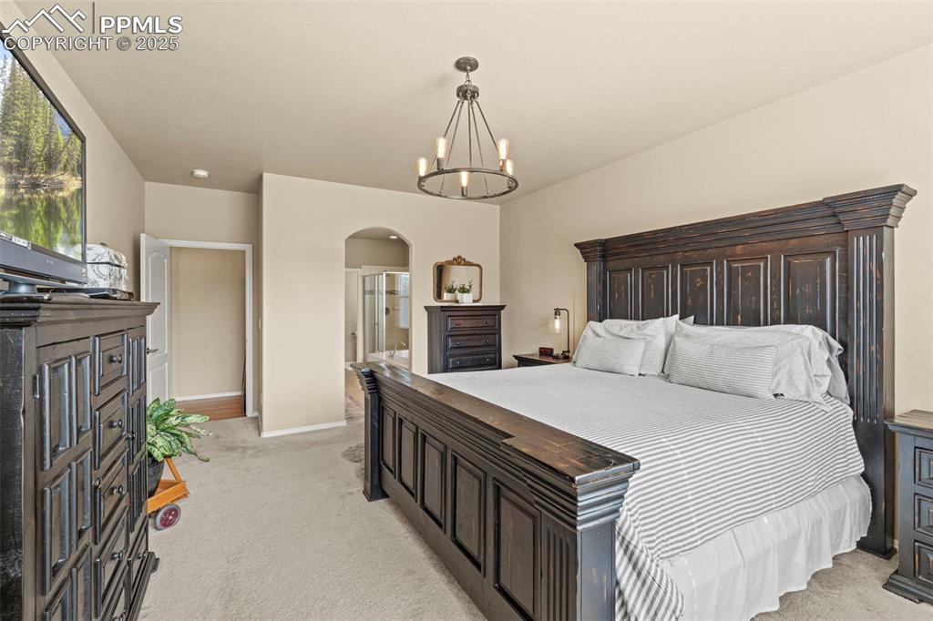 Image 25 of 44: Bedroom featuring light colored carpet, arched walkways, a chandelier, base