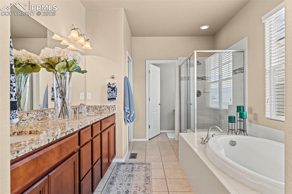 Image 27 of 44: Bathroom featuring a bath, double vanity, a shower stall, and tile patterne
