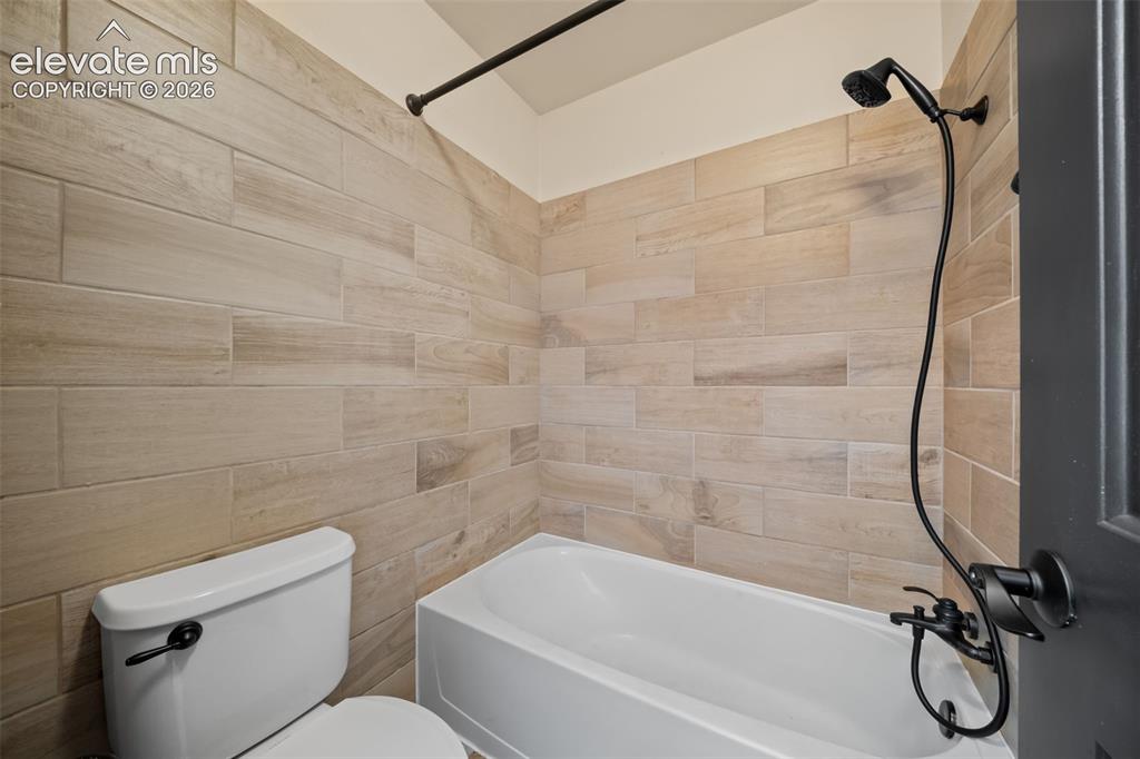 Image 28 of 48: Bathtub with tile surround, matte black shower fixtures, and white toilet