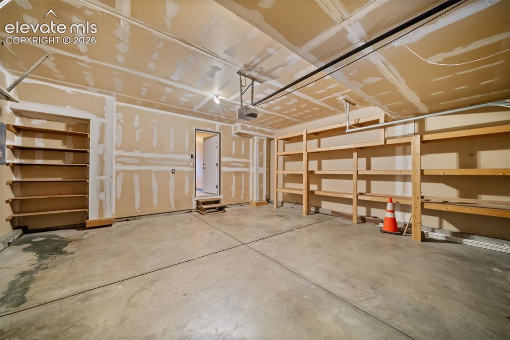 Image 36 of 48: Spacious garage featuring a concrete floor, built-in wooden shelving, and a