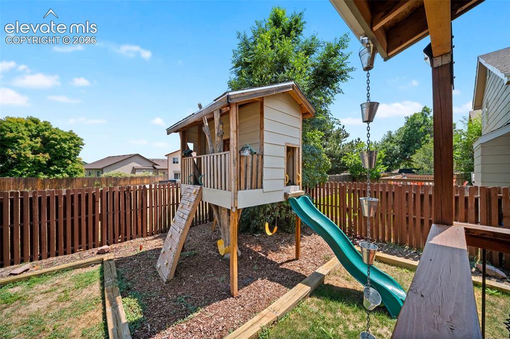 Image 38 of 48: Backyard featuring a built-in wooden play structure with a slide, a rain ch