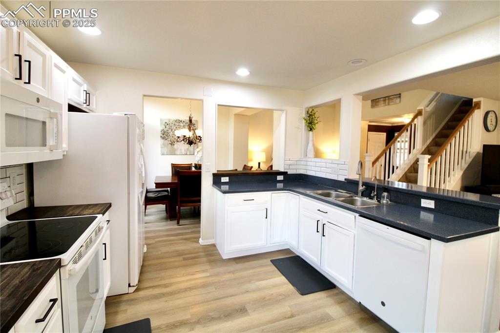 Image 15 of 50: Kitchen with white appliances, backsplash, a chandelier, white cabinetry, a