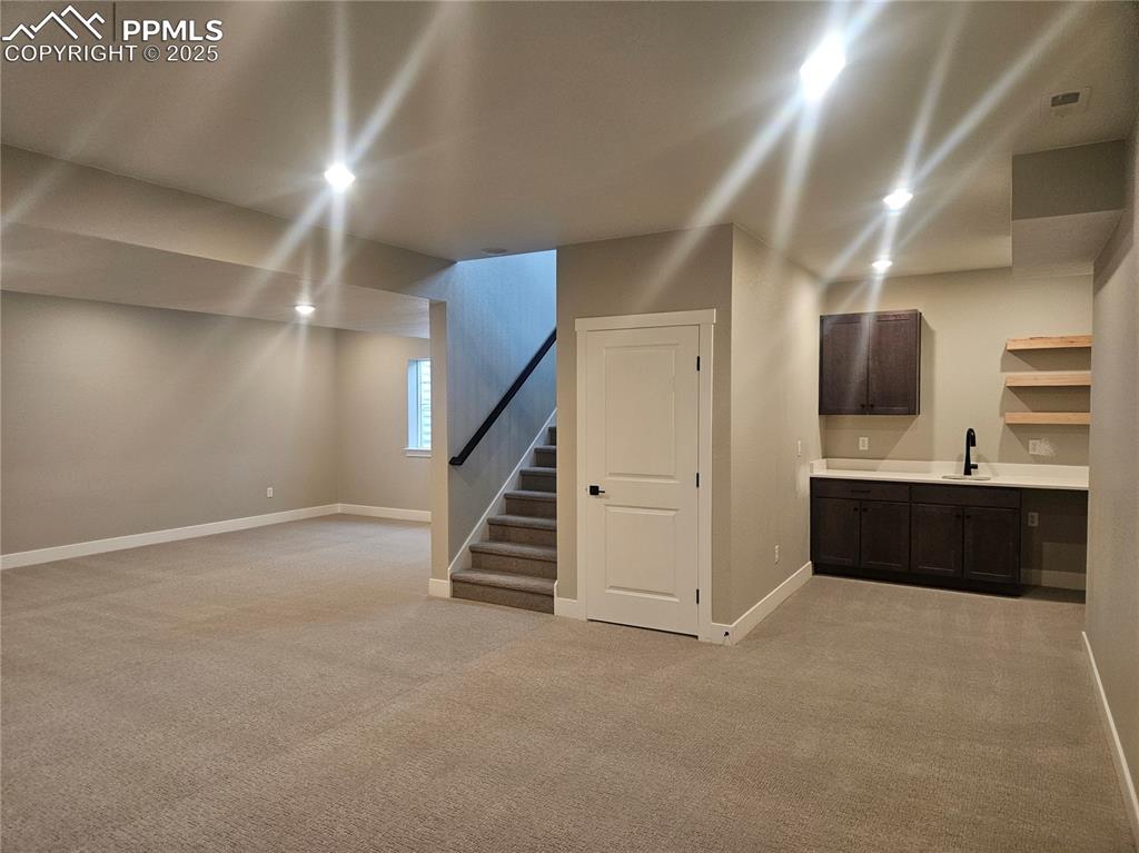 Image 15 of 15: Basement with light carpet, stairway, baseboards, and a sink