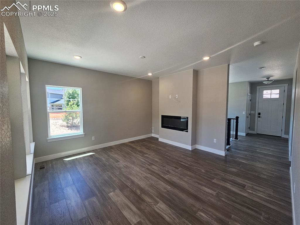 Image 9 of 15: Unfurnished living room with a textured ceiling, dark wood-style flooring, 