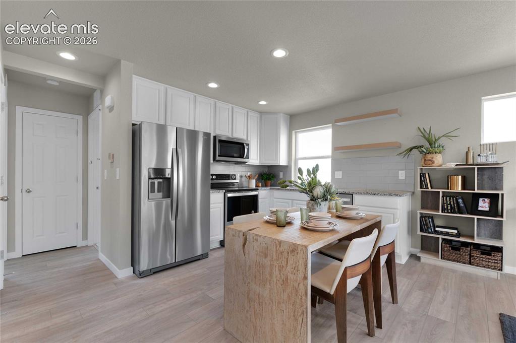 Image 13 of 31: Modern kitchen featuring stainless steel appliances, white cabinetry, a lig