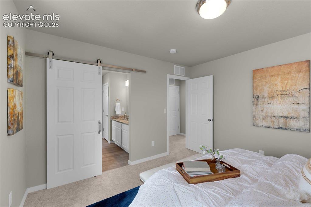 Image 19 of 31: Bedroom featuring a sliding barn door entryway to a bathroom with a vanity