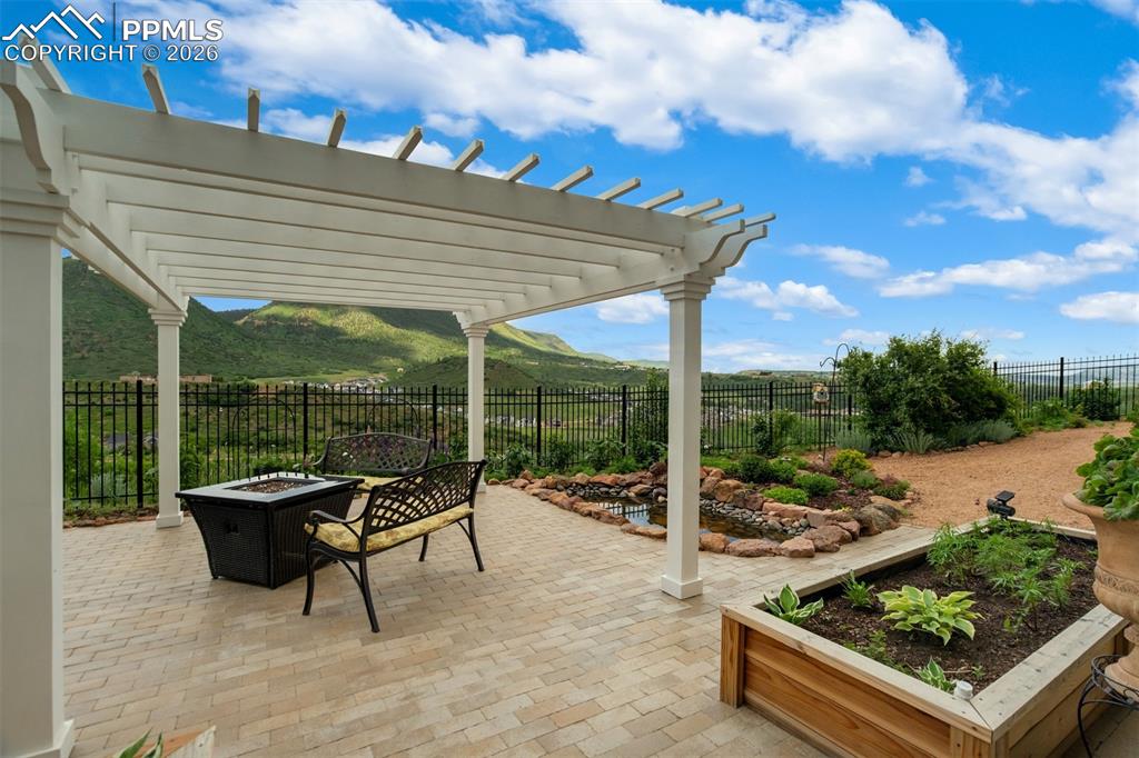 Image 30 of 40: Fully landscaped back yard with stone patio, pergola, and pond